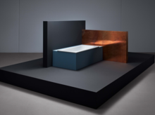 Rechteckige Badewanne aus Stahl-Email in moderner Umgebung, seitlich von dunklen und kupferfarbenen Wänden umgeben.