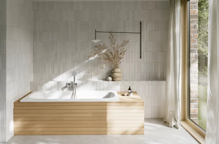 Weiße Badewanne aus glasiertem Titan-Stahl mit heller Verkleidung, weißer Fliesenwand und großem Fenster.