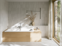 Weiße Badewanne aus glasiertem Titan-Stahl mit heller Verkleidung, weißer Fliesenwand und großem Fenster.