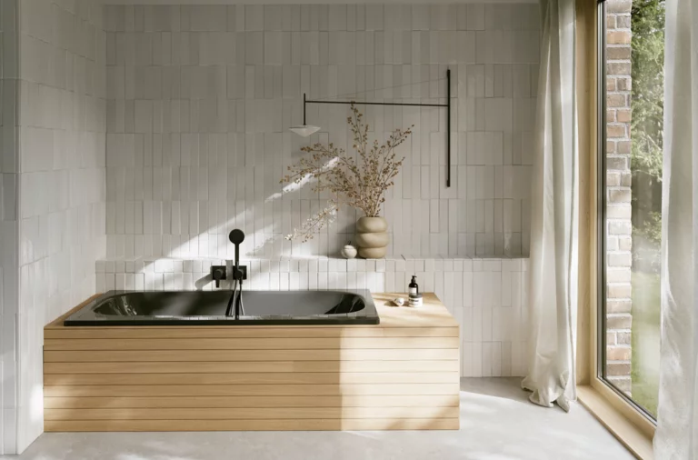 Schwarze Badewanne aus glasiertem Titan-Stahl mit heller Verkleidung, schwarzer Armatur und großem Fenster.