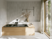 Schwarze Badewanne aus glasiertem Titan-Stahl mit heller Verkleidung, schwarzer Armatur und großem Fenster.