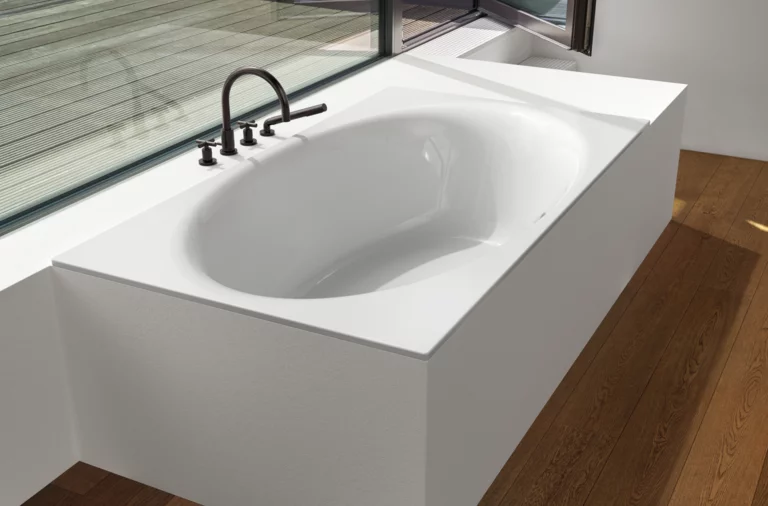 Rectangular steel enamel bathtub with oval interior, built into white paneling, fittings mounted on the side.