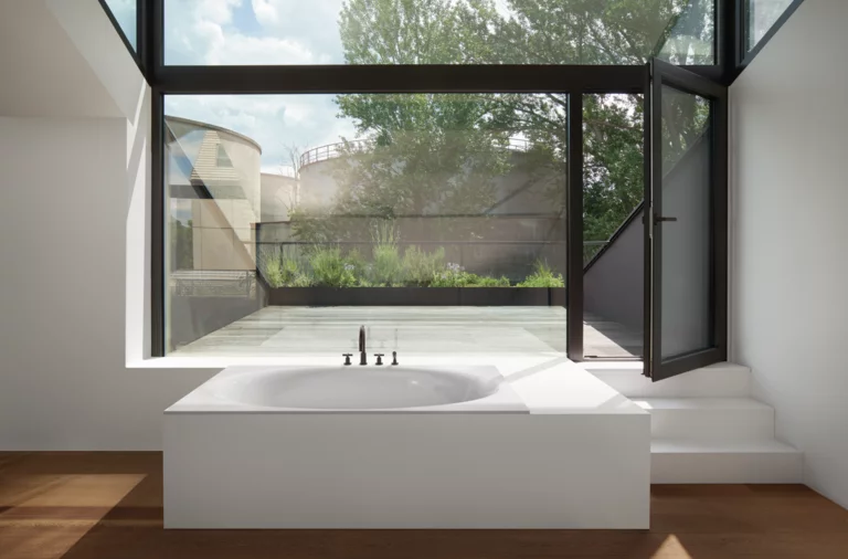 Rectangular steel-enamel bathtub with oval interior, freestanding in front of large windows, modern setting.