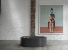 Freestanding oval bathtub in black, in front of white brick wall with artwork and exposed brick strip.