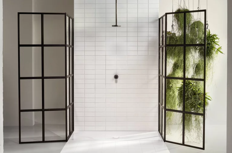 Plato de ducha cuadrado de acero esmaltado, azulejos blancos, mamparas de ducha negras, plantas verdes al fondo.