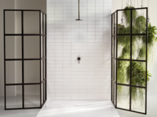 Plato de ducha cuadrado de acero esmaltado, azulejos blancos, mamparas de ducha negras, plantas verdes al fondo.