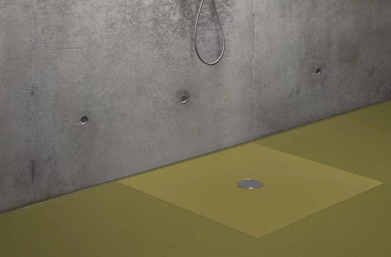 Plato de ducha rectangular de acero esmaltado en beige con desagüe central, a nivel del suelo frente a pared de hormigón.