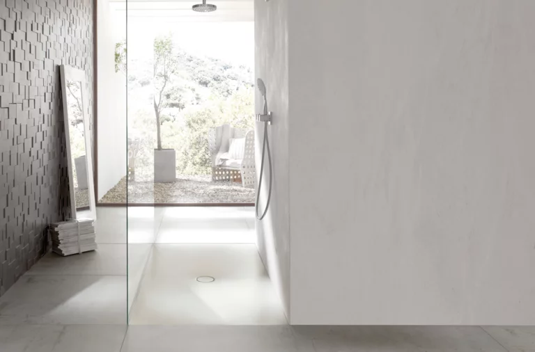 Plato de ducha rectangular de acero vitrificado con desagüe central, ducha a ras de suelo con mampara de cristal en baño moderno y luminoso.