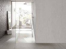 Plato de ducha rectangular de acero vitrificado con desagüe central, ducha a ras de suelo con mampara de cristal en baño moderno y luminoso.