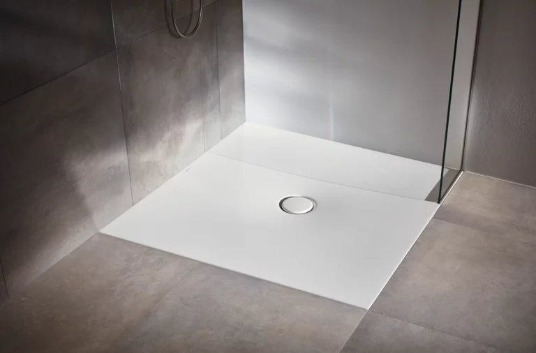 Plato de ducha rectangular de acero vitrificado con desagüe central, instalado a ras de suelo, rodeado de baldosas grises.