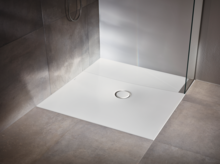 Plato de ducha rectangular de acero vitrificado con desagüe central, instalado a ras de suelo, rodeado de baldosas grises.