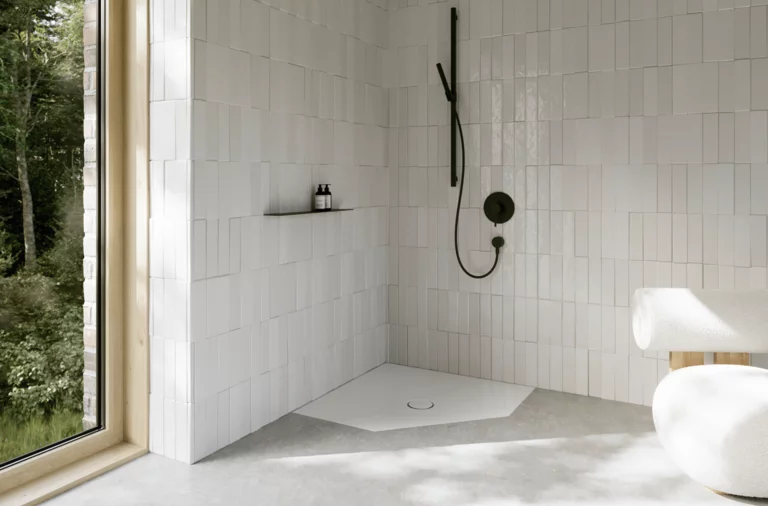 Witte vlakke vijfhoekige douchebak in een lichte badkamer met witte tegels, zwarte kranen en groot raam.
