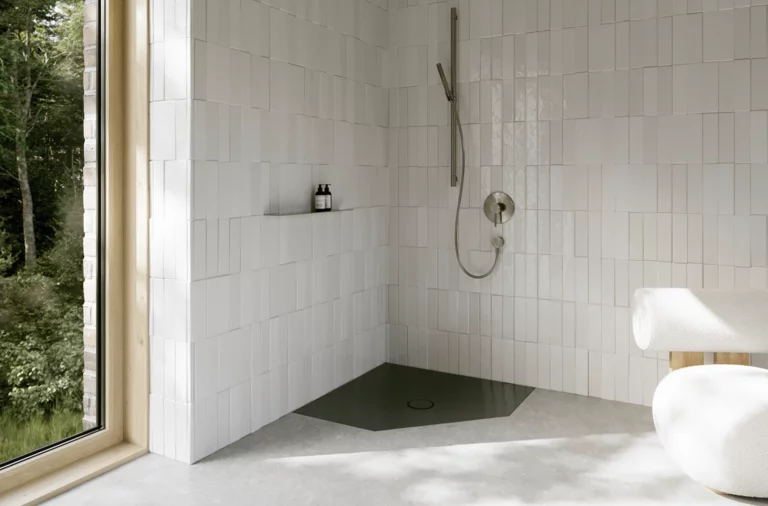 Donkere vlakke vijfhoekige douchebak in een lichte badkamer met witte tegels en groot raam.
