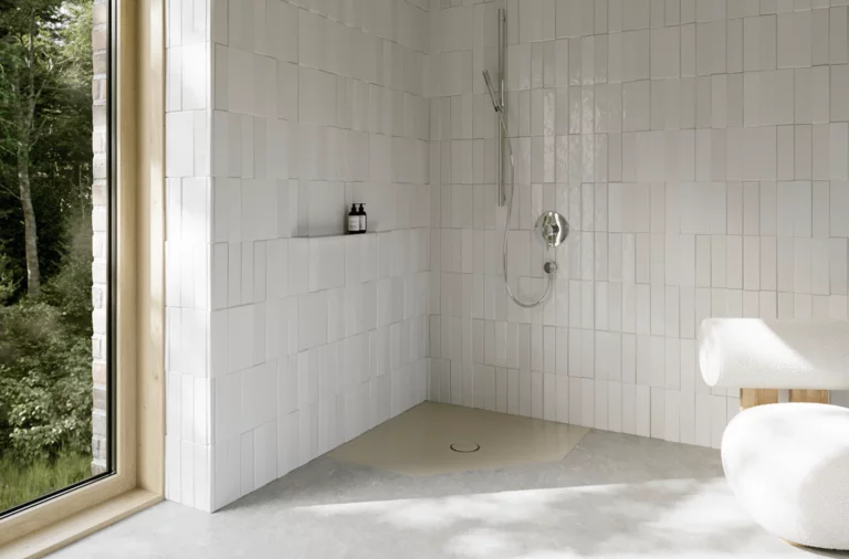 Lichte vlakke vijfhoekige douchebak in een wit betegelde badkamer met kraan en groot raam.