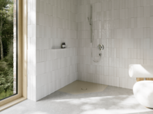 Lichte vlakke vijfhoekige douchebak in een wit betegelde badkamer met kraan en groot raam.