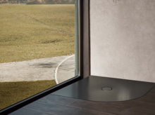 Superficie de ducha de acero vitrificado en color oscuro, forma redondeada y angular, a nivel del suelo frente a ventana y pared.