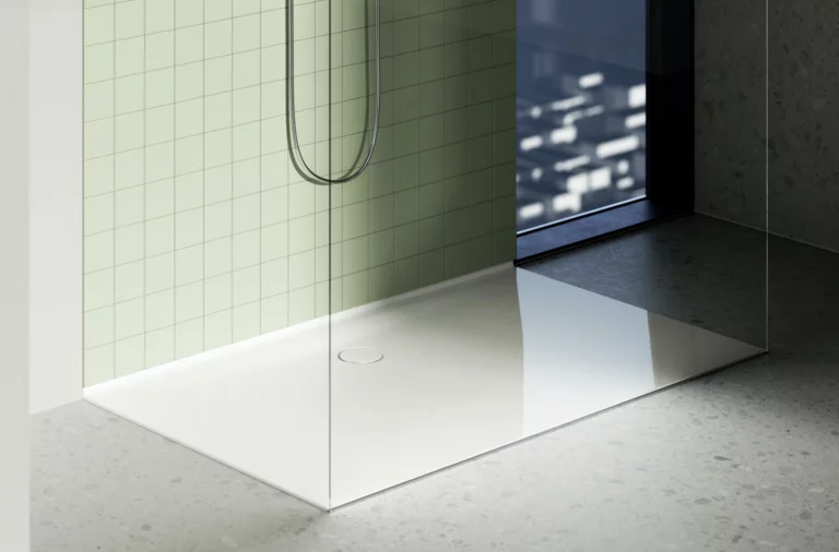 Weiße Duschwanne mit Glasduschabtrennung, grün gekachelter Wand und Blick auf die Stadt durch ein bodentiefes Fenster.