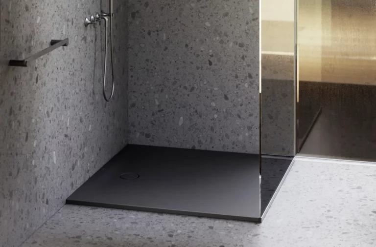 Современный душ с тёмным поддоном, стеклянной перегородкой и настенным смесителем в ванной с отделкой под камень.