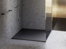 Современный душ с тёмным поддоном, стеклянной перегородкой и настенным смесителем в ванной с отделкой под камень.