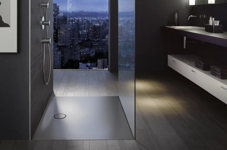 Barrierefreier Duschbereich mit rechteckiger Stahl-Email-Duschwanne und modernem Waschbecken auf Einbauplatte im dunklen Badezimmer.