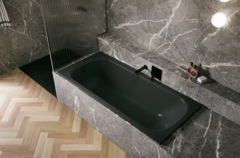 Bañera negra de acero titanio esmaltado en entorno gris efecto piedra, con grifo negro y suelo en espiga.