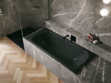 Bañera negra de acero titanio esmaltado en entorno gris efecto piedra, con grifo negro y suelo en espiga.