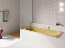 Bañera amarilla de acero titanio esmaltado en baño luminoso con azulejos blancos, grifo mural y ducha abierta.