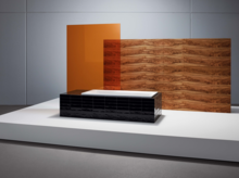Rechthoekig bad van staal-email, zwart bekleed, voor houten en oranje glazen wand op wit podium.
