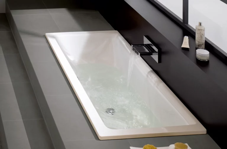 Rechthoekig bad van staal-email, deels gevuld met water, moderne watertoevoer, omgeven door grijze tegels.