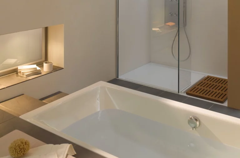 Rechthoekig bad en douchevloer van staal-email in moderne badkamer met glazen douchewand en plank.