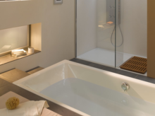 Rechthoekig bad en douchevloer van staal-email in moderne badkamer met glazen douchewand en plank.