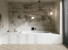 Minimalistisches Bad mit weißer eingelassener Badewanne, grauer Wandstruktur, Pendelleuchten und großem Fenster.