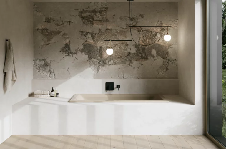 Minimalistisches Bad mit eingelassener beiger Badewanne, grauer Strukturwand, Pendelleuchten und großem Fenster.