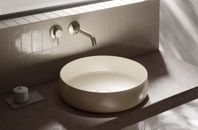 Ronde wastafel op inbouwblad, opbouwkraan aan betegelde wand, modern en minimalistisch badkamerontwerp.