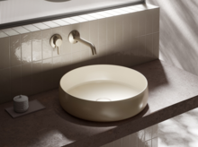 Ronde wastafel op inbouwblad, opbouwkraan aan betegelde wand, modern en minimalistisch badkamerontwerp.