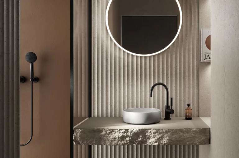 Rundes Waschbecken auf Einbauplatte aus Stein, runde Spiegelbeleuchtung, moderne Armatur, strukturierte Wand im Bad.