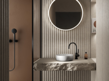 Rundes Waschbecken auf Einbauplatte aus Stein, runde Spiegelbeleuchtung, moderne Armatur, strukturierte Wand im Bad.