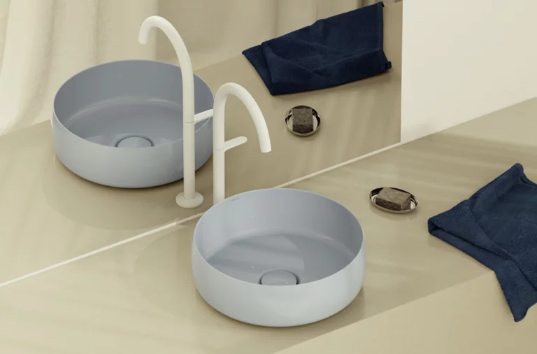 Moderne ronde opzetwastafel in lichtblauw op beige blad, met witte kraan, spiegel en donkerblauwe doekjes.