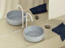 Moderne ronde opzetwastafel in lichtblauw op beige blad, met witte kraan, spiegel en donkerblauwe doekjes.