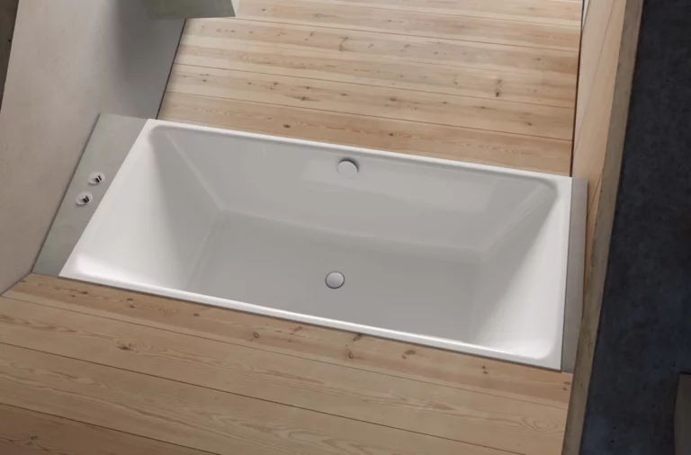 Rechteckige Badewanne aus Stahl-Email, in Holzfläche eingelassen, mit klaren Kanten und mittig angeordnetem Ablauf.