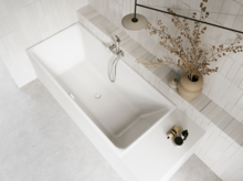 Weiße Badewanne in hellem Bad mit weißen Fliesen, Armatur, Handtuch und Vase mit Zweigen.
