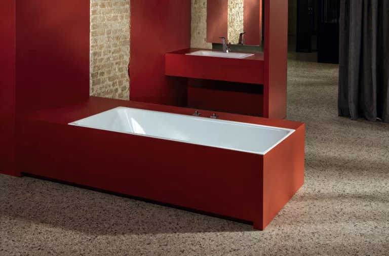 Rechteckige Badewanne aus Stahl-Email und rechteckiges Waschbecken auf Einbauplatte, beides mit roter Verkleidung.