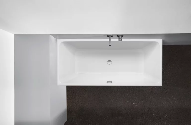 Rechteckige Badewanne aus Stahl-Email mit Ab- und Überlauf, eingebaut in dunklem Boden und heller Wand.