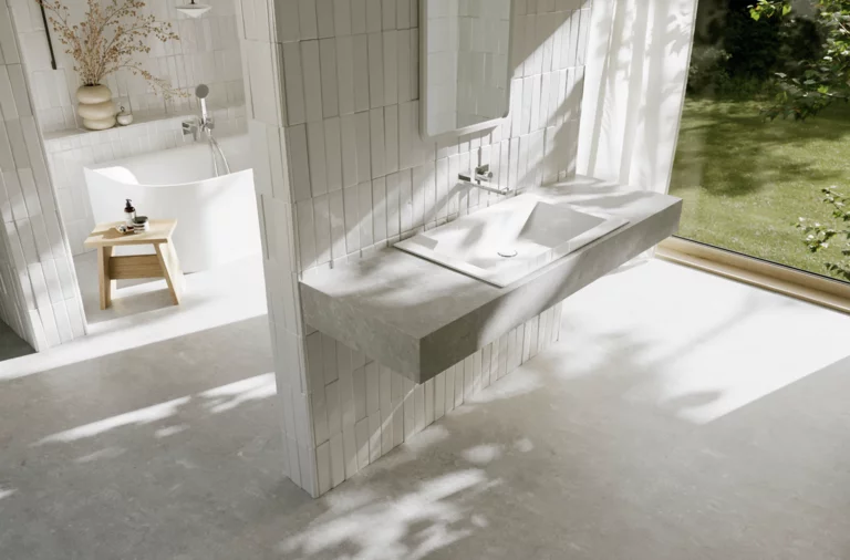 Bright bathroom with a white washbasin and integrated counter in front of a large window overlooking the green garden.