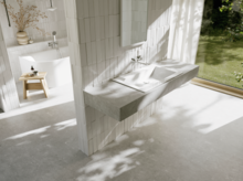 Bright bathroom with a white washbasin and integrated counter in front of a large window overlooking the green garden.