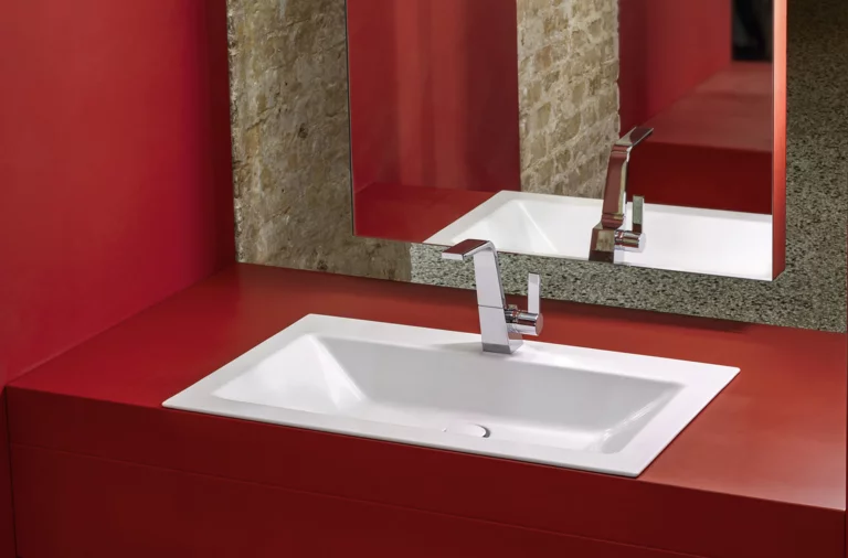 Rechteckiges Stahl-Email-Waschbecken in weiß, flächenbündig in rote Einbauplatte integriert, moderner Wasserhahn, großer Spiegel.