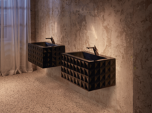 Dos lavabos rectangulares sobre encimeras con frente geométrico junto a pared rugosa, iluminación ambiental.