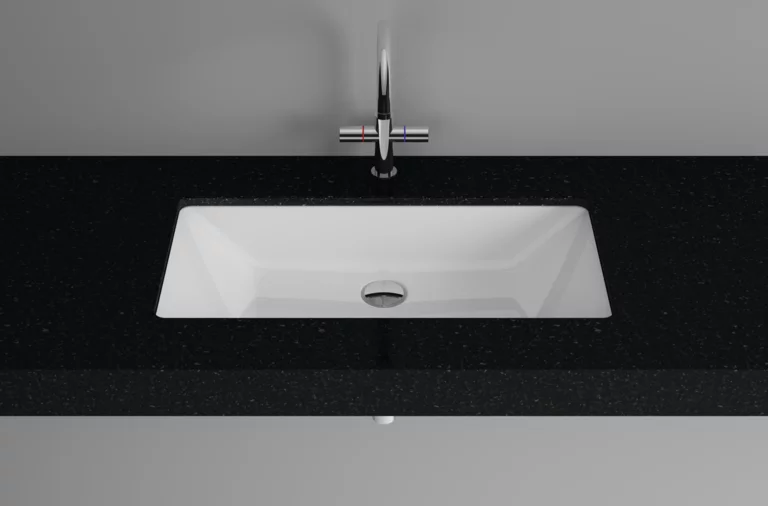 Rechteckiges Stahl-Email-Waschbecken in weiß, eingelassen in schwarze Einbauplatte, moderne Armatur darüber.