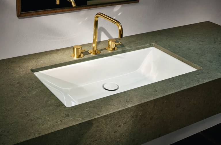 Rechteckiges Stahl-Email-Waschbecken in Einbauplatte, goldene Armatur, modernes Design, heller Hintergrund.