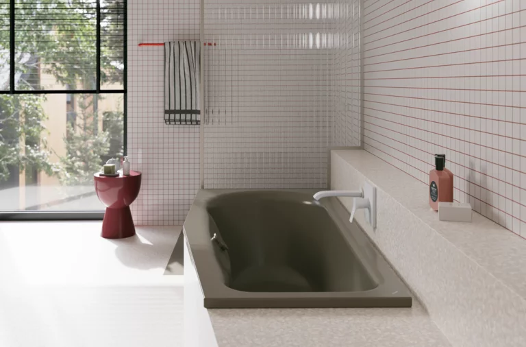 Olivgrüne Badewanne in hellem Bad mit weißen Fliesen, Fenster, rotem Hocker und Armatur.